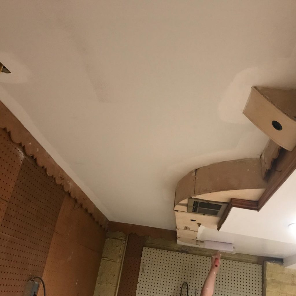 Basement with newly installed ceiling covering ductwork, pegboard wall, and a person reaching up.